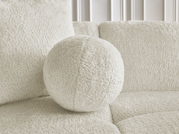 Gros plan d'un coussin rond matelassé du canapé Cristina blanc crème.