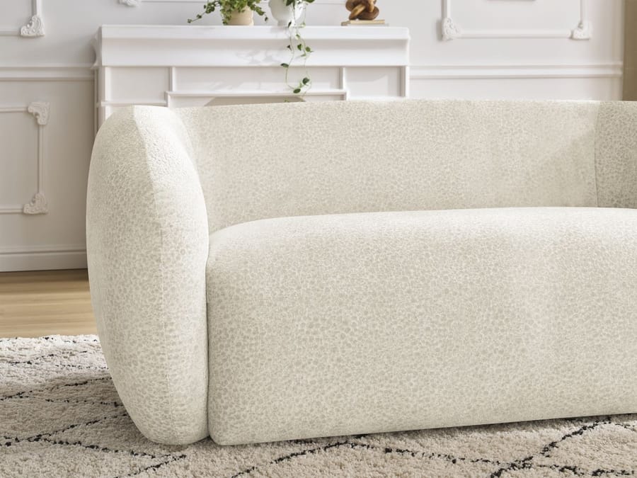 Vue rapprochée du profil et de l'accoudoir du canapé Celine en tissu beige.