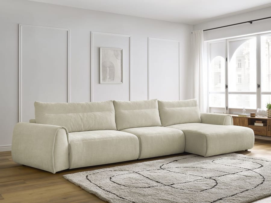 Canapé Aden d'angle beige dans un salon blanc avec tapis gris et accoudoirs visibles