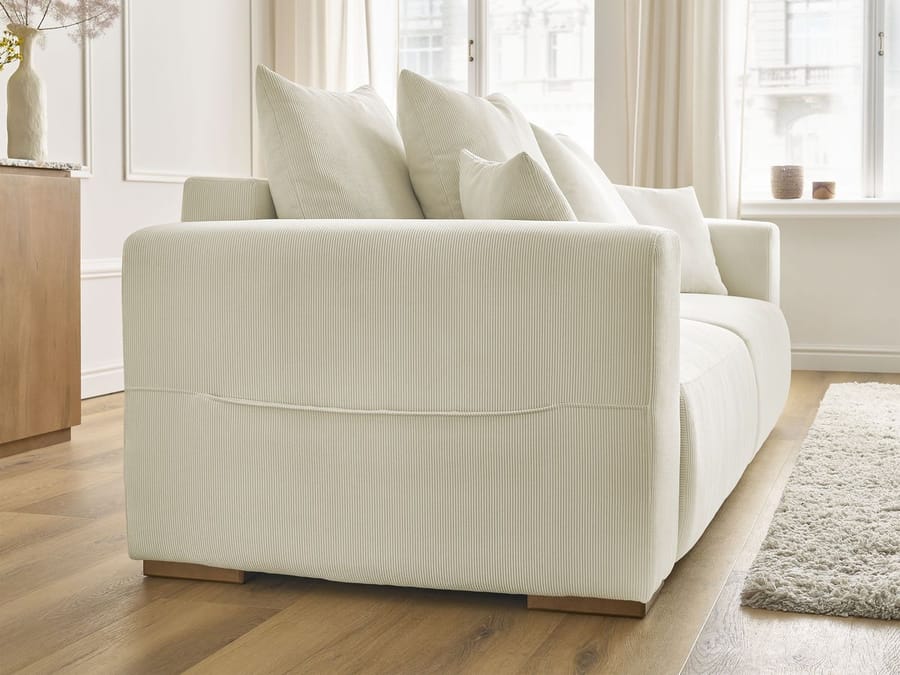 Canapé Sidonie beige côté droit, profondeur visible, coussins empilés dessus
