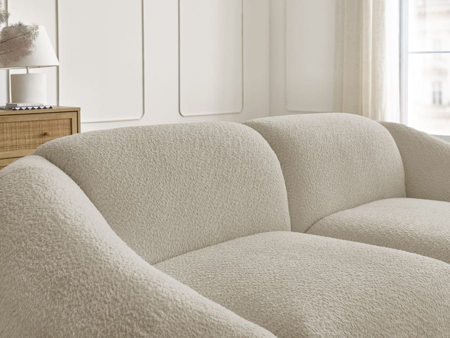Gros plan des accoudoirs arrondis du canapé Tina en tissu beige.