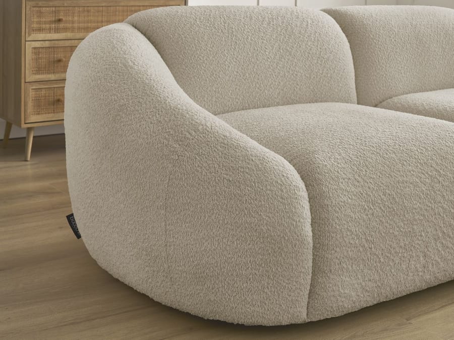 Gros plan de l accoudoir arrondi du canapé Tina en tissu beige clair.