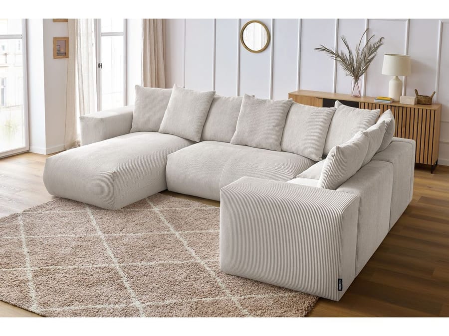 Canapé Voltaire d'angle en tissu beige clair dans un salon blanc avec fenêtres et mobilier bois
