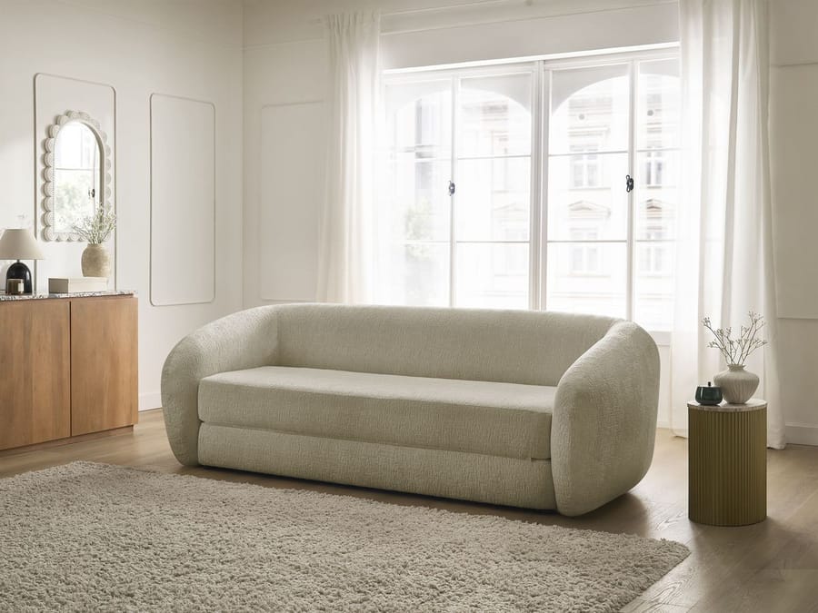 Canapé Neyo convertible beige dans un salon blanc avec fenêtres, miroir et rangements.