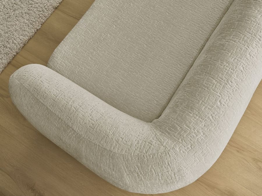 Gros plan de l'accoudoir arrondi du canapé Neyo en tissu beige texturé.