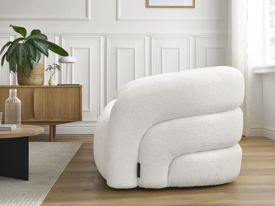Fauteuil Elina blanc arrondi dans un salon moderne, meuble en bois, plante.