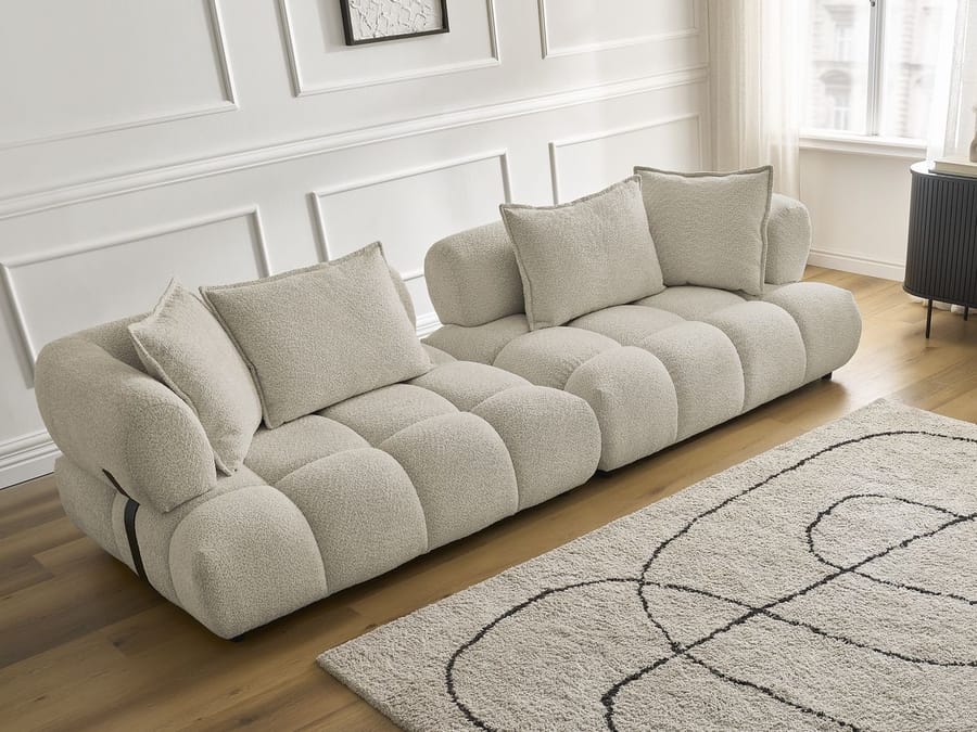Canapé Alya en tissu beige clair vu de profil bas, montrant les coussins arrondis et les pieds.