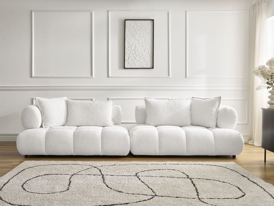 Canapé Alya en tissu blanc crème dans un salon clair avec mur blanc lambrissé et tapis.