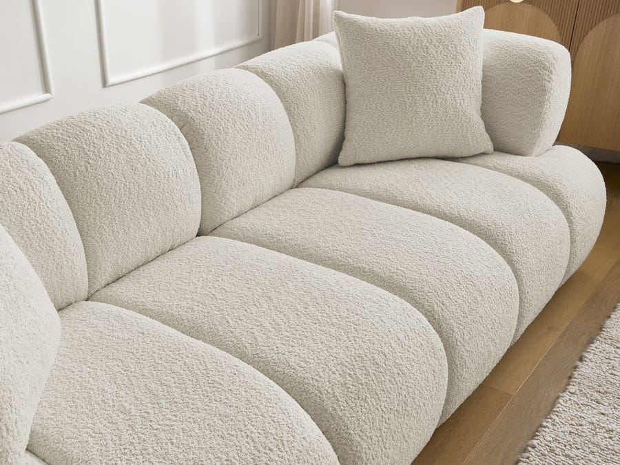Gros plan du canapé Pamira beige montrant le capitonnage arrondi et les coussins de décoration