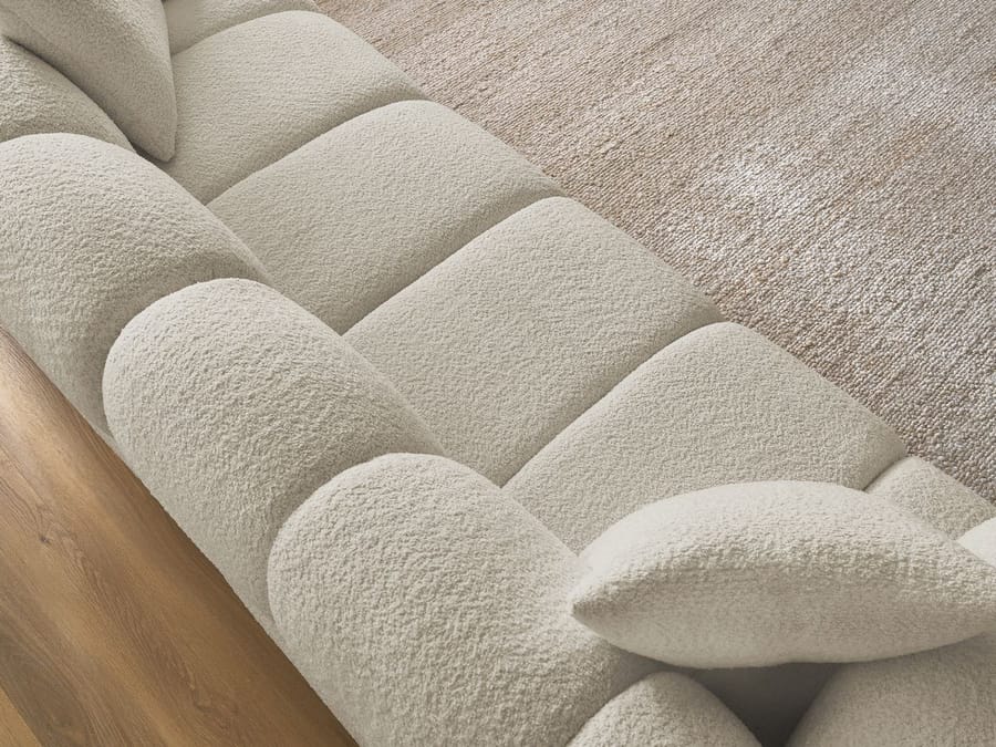 Gros plan de la matière bouclette beige du canapé Pamira et du capitonnage détaillé