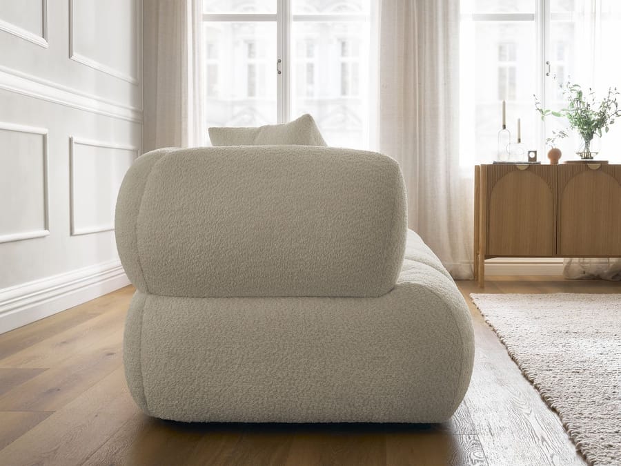 Canapé Pamira beige vu de l'arrière, montrant la forme arrondie, salon blanc avec fenêtre