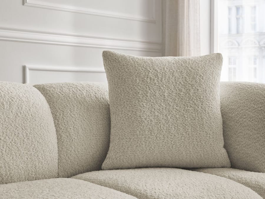 Gros plan des coussins de décoration du canapé Pamira en tissu bouclette beige clair