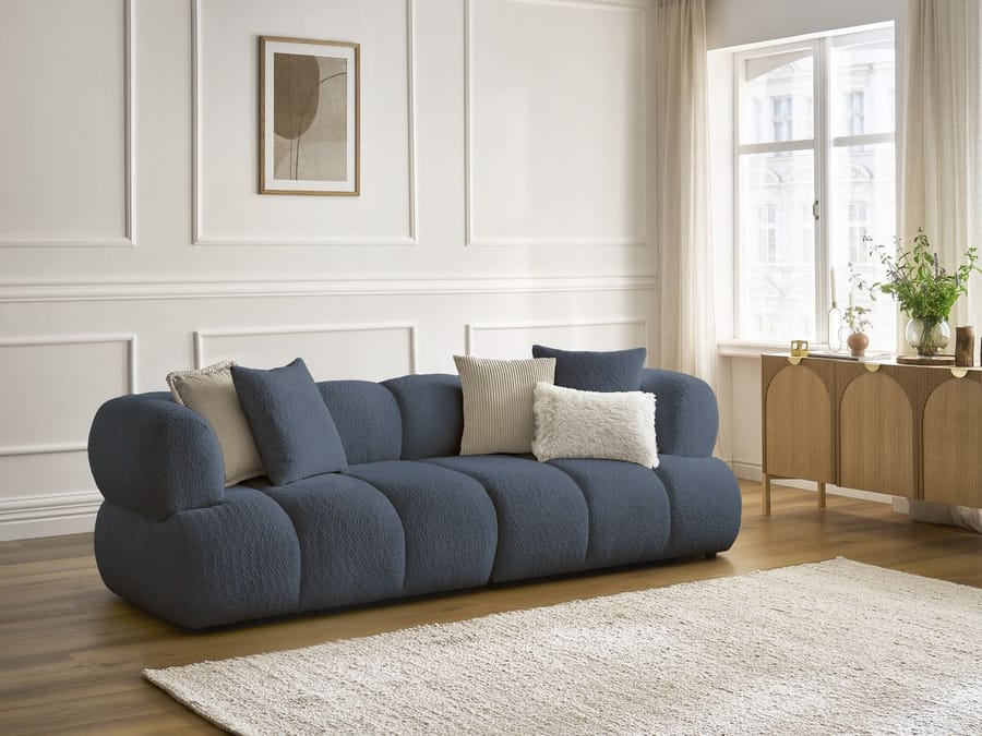 Canapé Pamira bleu foncé dans un salon blanc avec fenêtres, meuble bois et tapis